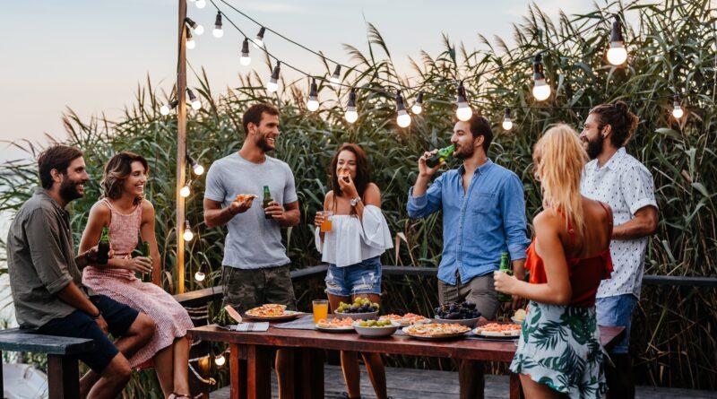 Freunde genießen Essen und Getränke im Garten unter Lichterkette | Terrassenüberdachung