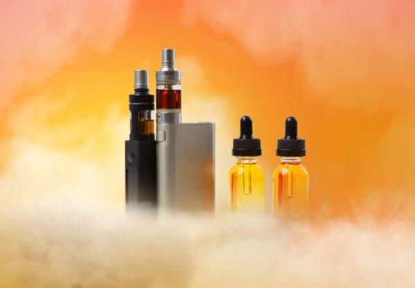 Elfliq Mini Liquids und E-Zigaretten vor orangefarbenem Hintergrund mit Dampf